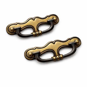 Op de afbeelding: Twee handgrepen in antieke stijl. Elke handgreep heeft een gebogen, donkerbronzen handvat dat is bevestigd aan een decoratieve, goudkleurige achterplaat. De achterplaten hebben een geschulpte rand en zijn gemonteerd met kleine, ronde bronzen accenten.