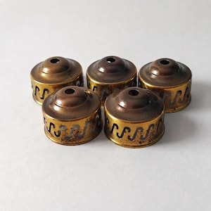 May include: Five vintage brass lamp shades with a decorative wavy pattern around the base. The shades have a dark brown top and a gold-colored base. The shades are arranged in a circular pattern on a white surface.