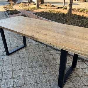 Könnte beinhalten: Ein langer Holztisch mit natürlicher Oberfläche und schwarzen Metallbeinen. Der Tisch steht auf einer grauen Steinplatte.