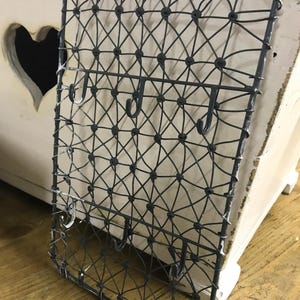 Könnte beinhalten: Ein schwarzer Wandorganizer aus Metalldraht mit mehreren Haken. Der Organizer hat ein Rautenmuster und ist ideal zum Aufhängen von Schlüsseln, Schmuck oder anderen kleinen Gegenständen.