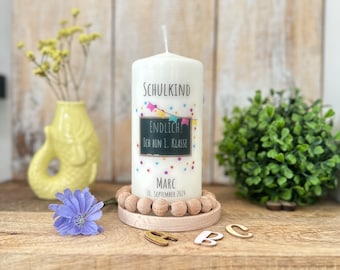 Può includere: Candela bianca con un design colorato che presenta una lavagna con il testo "Endlich! Ich bin 1. Klasse" e il nome "Marc" e la data "30. September 2024". La candela è su una base di legno con perline di legno.