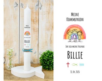 Può includere: Una candela bianca da comunione con il testo "Meine Kommunion" e "Billie" stampato sopra. La candela ha un'illustrazione di arcobaleno e bambini. È posta su un supporto bianco a forma di pesce e legata con un nastro blu.