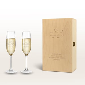 Può includere: Due flûte di champagne piene di liquido frizzante, accanto a una scatola di legno. Le flûte hanno un cuore e il testo "ANOUK & HEATH 12.11.2025". La scatola ha lo stesso design e testo.