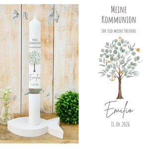 Könnte beinhalten: Eine weiße Kommunionkerze mit dem Text "Meine Kommunion" und "Ihr seid meine Freunde", einer Baumillustration, dem Namen "Emilio" und dem Datum "11.04.2026". Die Kerze steht in einem weißen, fischförmigen Halter.
