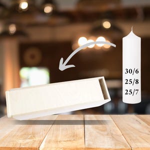 May include: A white wooden box with a white pillar candle. The candle is labeled with the numbers 30/6, 25/8, and 25/7. The box is tilted to the side, and the candle is standing upright.