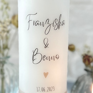 May include: White candle with the names Franziska & Benno and the date 17.06.2023 printed on it. A small heart is printed below the names.