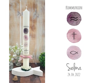 May include: White communion candle with a pink ribbon and a white fish, cross, and wavy lines design. The candle is decorated with the name Selma and the date 24.04.2022. The candle is on a white fish-shaped stand.