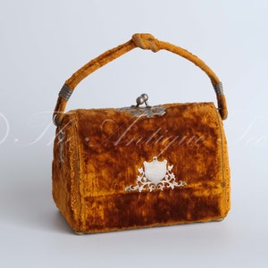 May include: A vintage velvet handbag with a knotted handle and a silver clasp. The bag is a rich brown color and has a silver shield design on the front.