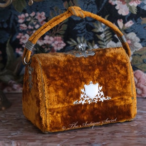 May include: A small, vintage, mustard yellow velvet handbag with a silver clasp and ornate silver design. The bag has a top handle and is in good condition.