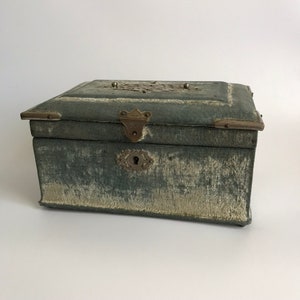 May include: A vintage green fabric-covered box with brass hardware, including a lock and hinges. The top of the box has a decorative metal design.