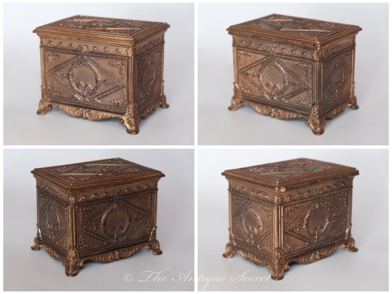 Puede incluir: Una peque&ntilde;a caja de madera antigua adornada con una tapa con bisagras. La caja est&aacute; hecha de madera oscura y tiene tallas intrincadas en la parte delantera y los lados. La caja est&aacute; decorada con un acabado dorado y tiene un dise&ntilde;o decorativo en la tapa.