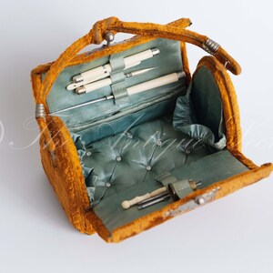 May include: An antique yellow velvet sewing kit with a blue satin lining and a variety of sewing tools, including needles, thread, and a thimble.