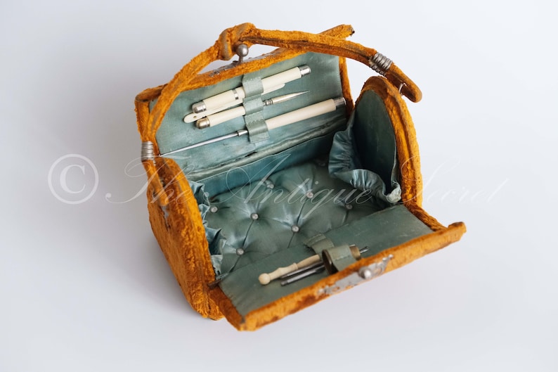 May include: An antique yellow velvet sewing kit with a blue satin lining and a variety of sewing tools, including needles, thread, and a thimble.