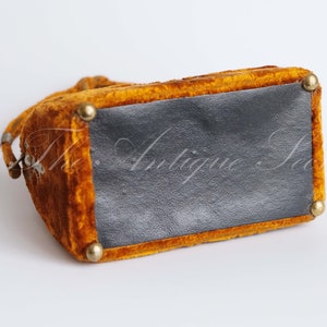 May include: A small, mustard yellow velvet handbag with a black fabric lining and gold metal accents. The bag has a top handle and a clasp closure.