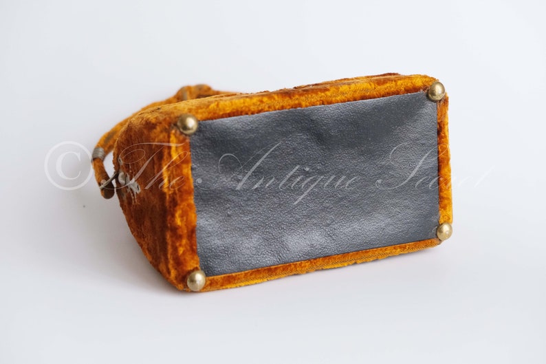 May include: A small, mustard yellow velvet handbag with a black fabric lining and gold metal accents. The bag has a top handle and a clasp closure.