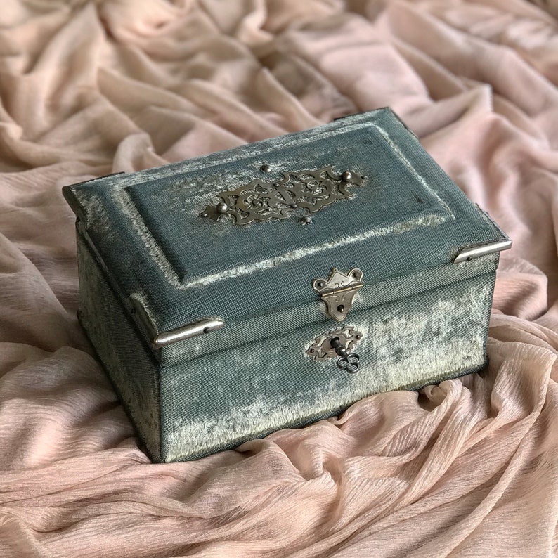 May include: A vintage green velvet jewelry box with a silver metal latch and ornate design. The box has a keyhole and a tarnished silver metal design on the lid.