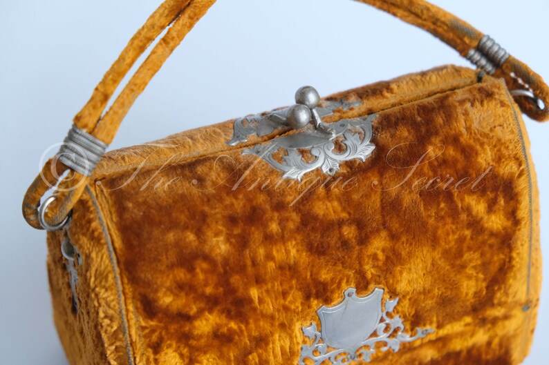May include: A vintage velvet handbag with a silver clasp and ornate metal accents. The bag is a rich mustard yellow color.