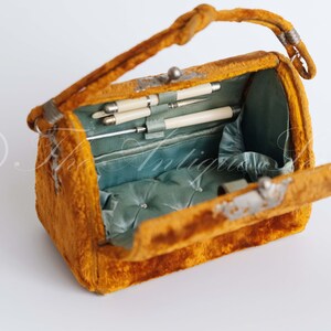 May include: An antique velvet handbag with a hinged lid, open to reveal a blue satin interior with a padded cushion and several silver-tipped tools.