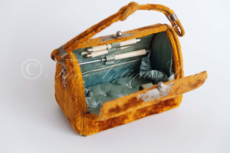 May include: An antique velvet handbag with a hinged lid, open to reveal a blue satin interior with a padded cushion and several silver-tipped tools.