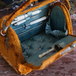 May include: An antique velvet vanity case with a blue satin lining. The case is open and reveals a set of silver-plated tools, including a small pair of scissors, a tweezers, and a nail file.