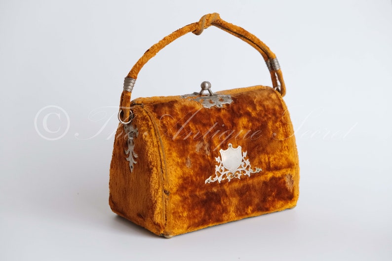 May include: A vintage velvet handbag with a silver clasp and ornate metal accents. The bag is a rich orange color and has a top handle.