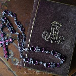 May include: A vintage velvet-covered book with a silver monogram and a cross-shaped necklace with pink and clear glass stones.