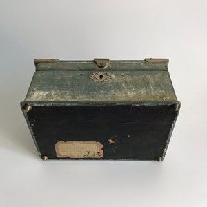May include: A vintage green fabric covered box with brass hardware and a keyhole. The box has a label on the bottom that reads "Made in England by J.W. Benson Ltd."