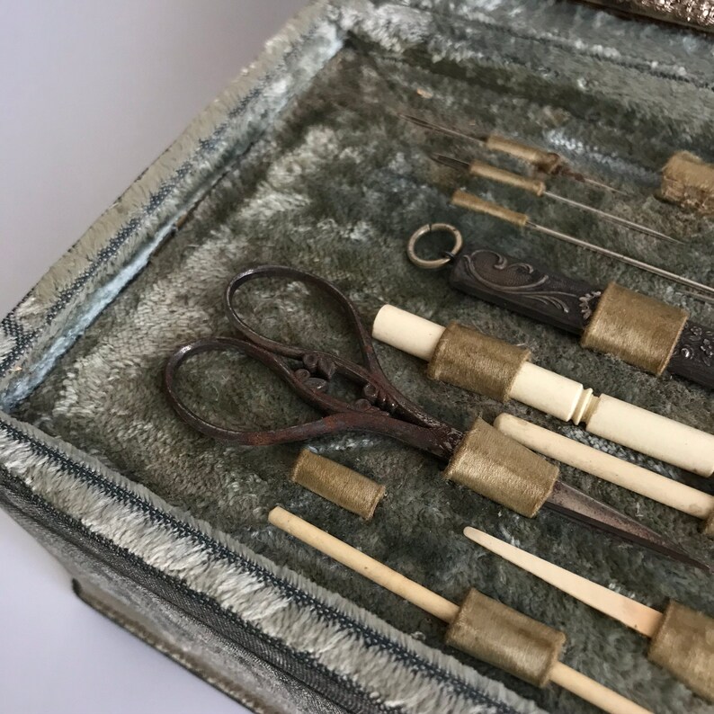 May include: A vintage sewing kit with a variety of tools, including scissors, needles, and thimbles. The tools are arranged in a velvet-lined box.