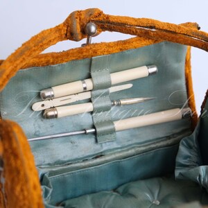 May include: An open vintage orange velvet vanity case with a blue satin lining. The case contains a set of ivory handled tools, including a pair of tweezers, a small knife, and a small brush.