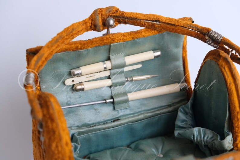 May include: An open vintage orange velvet vanity case with a blue satin lining. The case contains a set of ivory handled tools, including a pair of tweezers, a small knife, and a small brush.