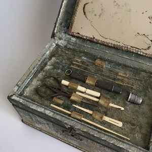 May include: An antique sewing kit with a green velvet lining. The kit includes a pair of scissors, a thimble, needles, and a small mirror.
