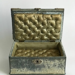 May include: A vintage gray velvet jewelry box with a tufted interior and a brass lock and keyhole.