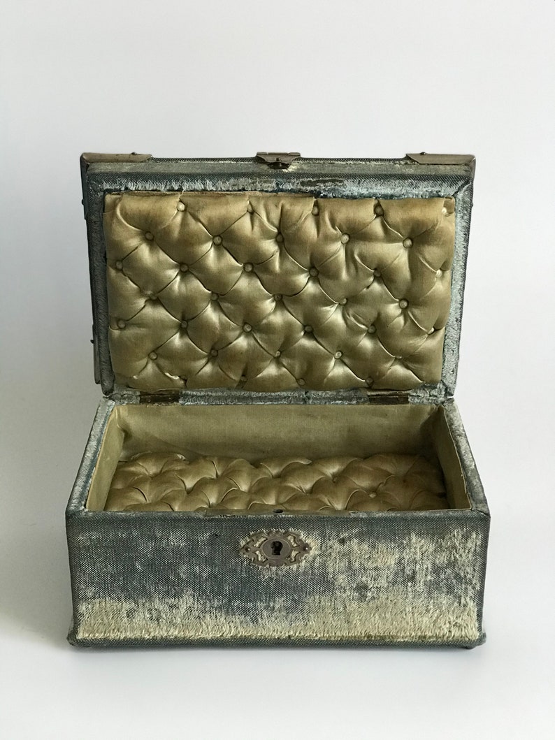 May include: A vintage gray velvet jewelry box with a tufted interior and a brass lock and keyhole.
