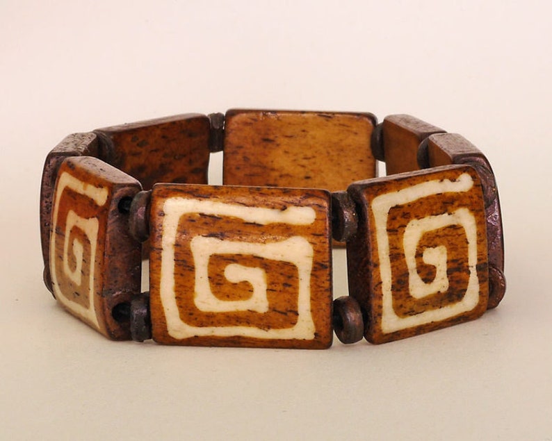 Puede incluir: Un brazalete de madera marr&oacute;n con dise&ntilde;os en espiral blancos en cada una de las cuentas cuadradas.