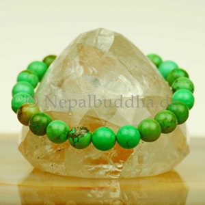 May include: A green gemstone bracelet with round beads. The bracelet is displayed on a clear quartz crystal.