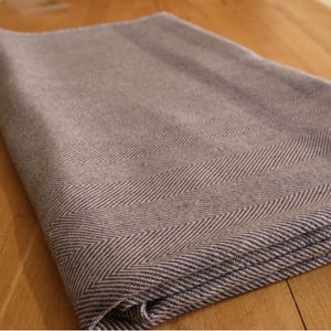 May include: A folded, gray blanket with a herringbone pattern border. The blanket is a muted gray color with a darker gray and white chevron design along the edge. The blanket is made of a soft material.