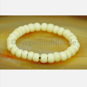 May include: A white beaded bracelet with a gold clasp. The bracelet is made of small, round beads and is approximately 7 inches in length.