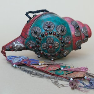 Peut inclure: Un coquillage décoratif avec un extérieur turquoise et rouge, orné de métal ouvragé et d'accents de bijoux. Une gland en tissu coloré est attaché à la coquille. La coquille a une poignée noire.