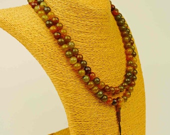 May include: A multi-colored beaded necklace with green, brown, and orange beads. The necklace is displayed on a yellow mannequin.