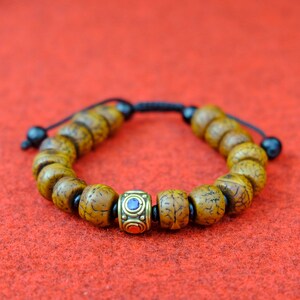 May include: A brown wooden bead bracelet with a gold and blue decorative bead in the center. The bracelet is on a red surface.