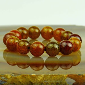 May include: A bracelet made of round, brown, orange, and green agate beads. The beads have a natural, marbled pattern.