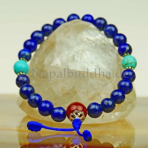 May include: A blue lapis lazuli mala prayer bead bracelet with turquoise and red carnelian beads. The bracelet has a silver charm and a blue cord.