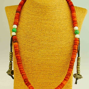 May include: A long necklace made of red, white, and green beads. The necklace is on a brown mannequin. The beads are made of wood and stone.
