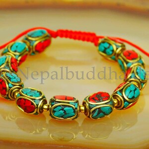 May include: A red string bracelet with turquoise and red beads. The beads are made of metal and have a gold finish. The bracelet is tied with a knot and has a tassel.
