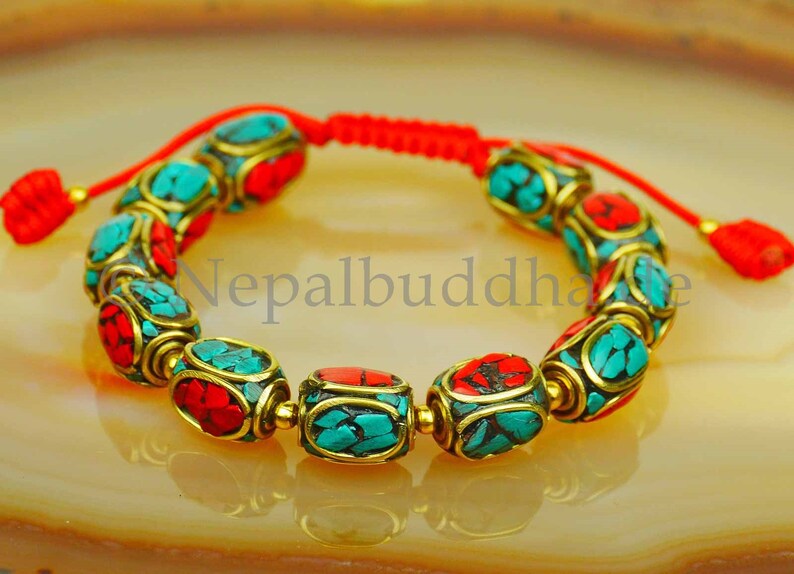 May include: A red string bracelet with turquoise and red beads. The beads are made of metal and have a gold finish. The bracelet is tied with a knot and has a tassel.