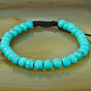 May include: Turquoise beaded bracelet with a black cord and adjustable closure. The bracelet is made of round beads with a smooth, polished finish.