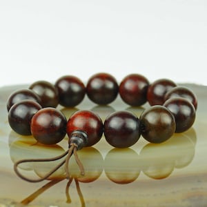 May include: A dark brown wooden beaded bracelet with a brown cord tassel. The beads are round and smooth, and the bracelet is made of natural wood.