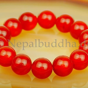 May include: A red carnelian gemstone bracelet with 14 round beads. The bracelet is on a light yellow background.