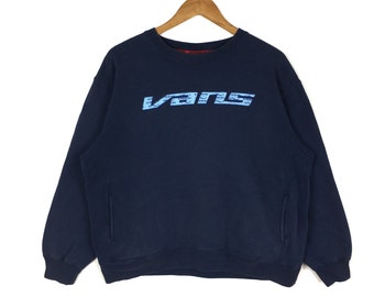 Puede incluir: Una sudadera azul marino con un logotipo Vans azul claro estampado en la parte delantera. El logotipo está formado por la palabra "Vans" repetida varias veces.