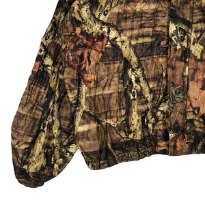 May include: A brown, green, and tan camouflage jacket with a button-up front. The jacket has a relaxed fit and a slightly cropped length.